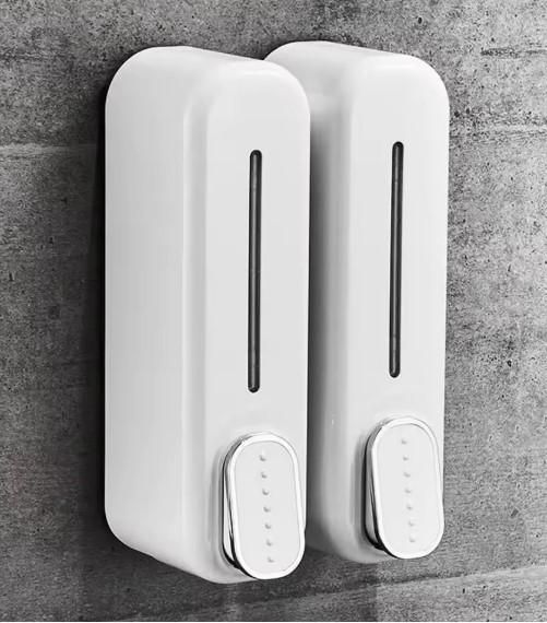 White plastic manual wall-mounted soap dispensers installed on a gray concrete wall with visible liquid level indicators.