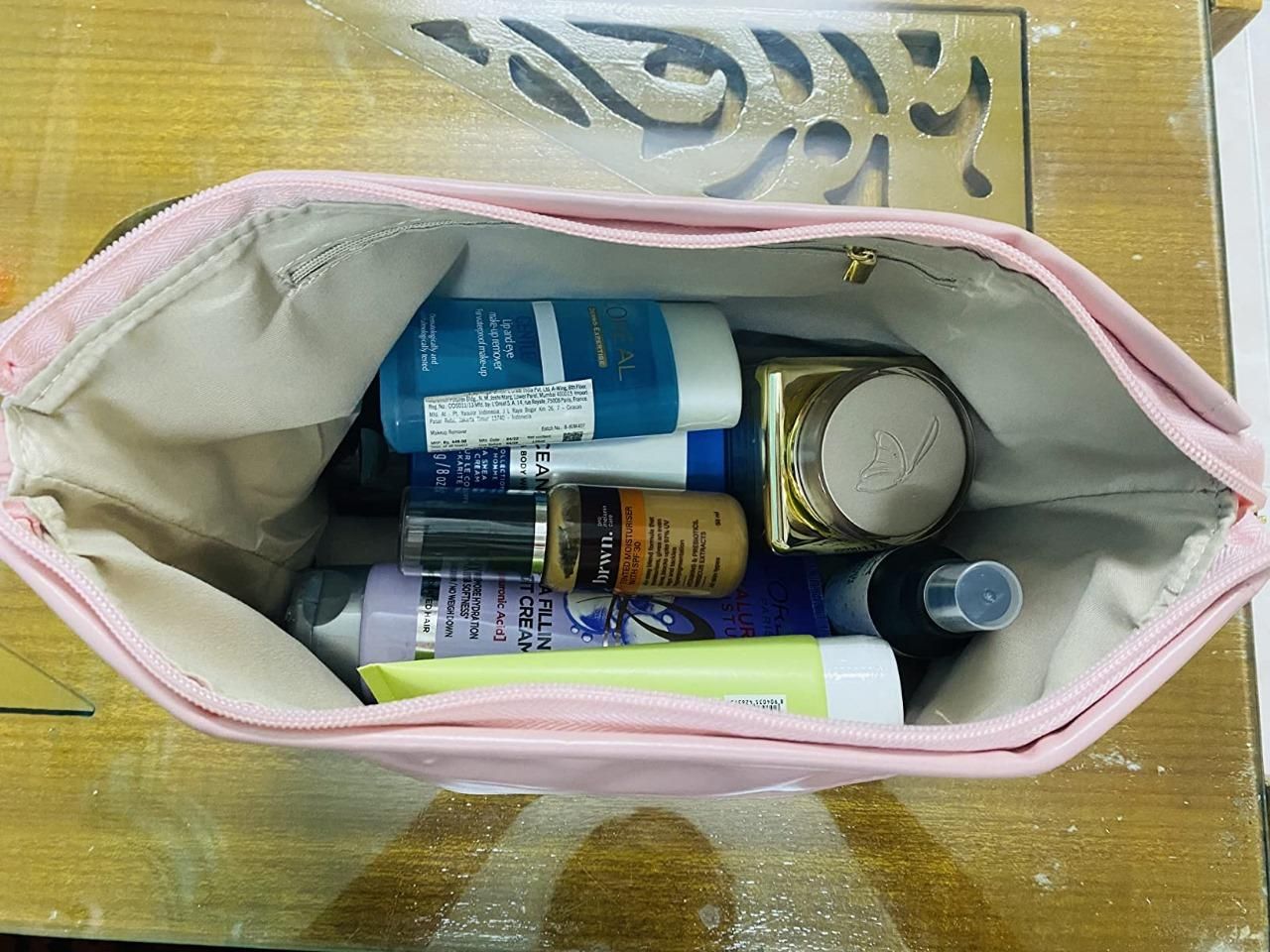 large capacity cosmetic travel bag in pink with makeup and skincare products inside viewed from above