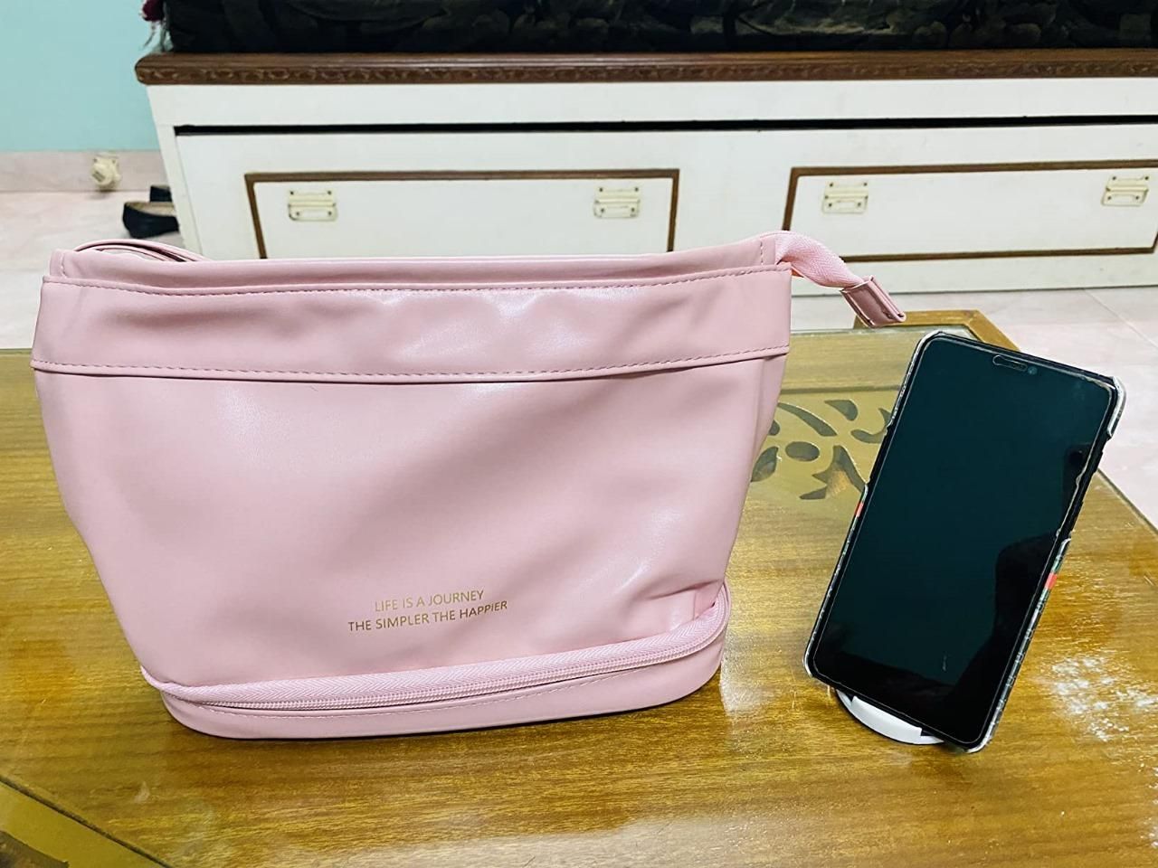 Pink large capacity cosmetic travel bag with zipper and handle next to a smartphone on a wooden table