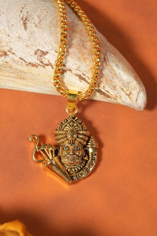 Golden Khatu Shyamji pendant with chain made of stainless steel and gold plated, displayed on a beige textured surface.
