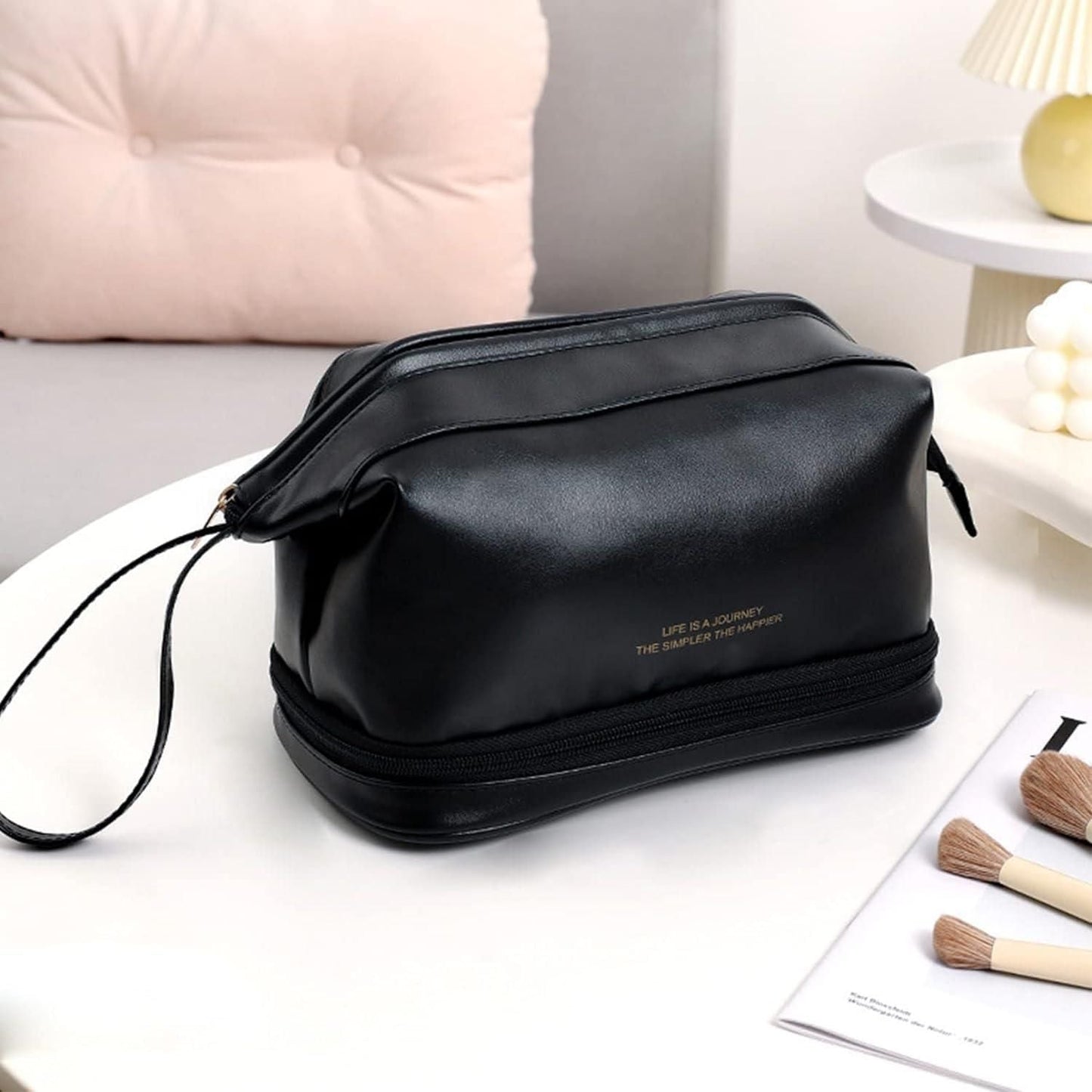 Black large capacity cosmetic travel bag with zipper and handle on white table with makeup brushes nearby