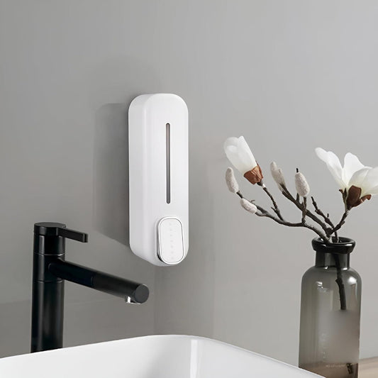 White plastic wall-mounted manual soap dispenser installed above sink with modern black faucet and decorative flowers in a vase nearby